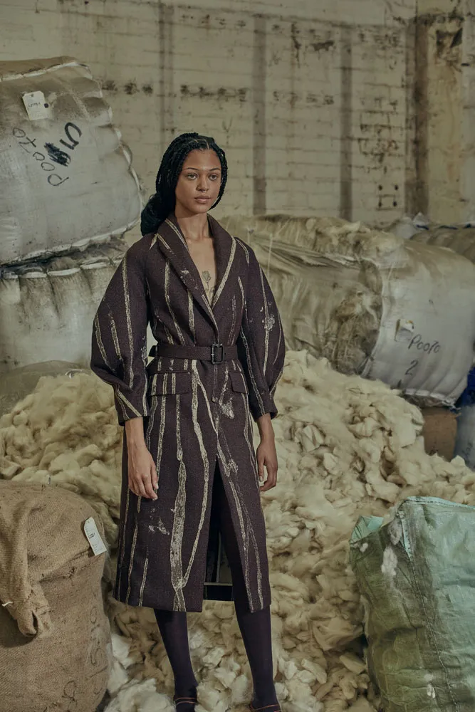 Model in a hand-tailored striped wool coat photographed among raw wool bales